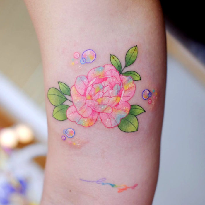 Tatuadora crea tatuajes delicados; tatuaje de flor peonia en tonos pastel en el brazo