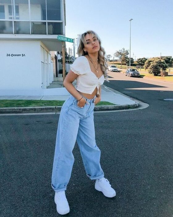 chica con jeans azules holgados y crop top blanco; 13 Ideas para usar pantalones holgados sin perder el estilo
