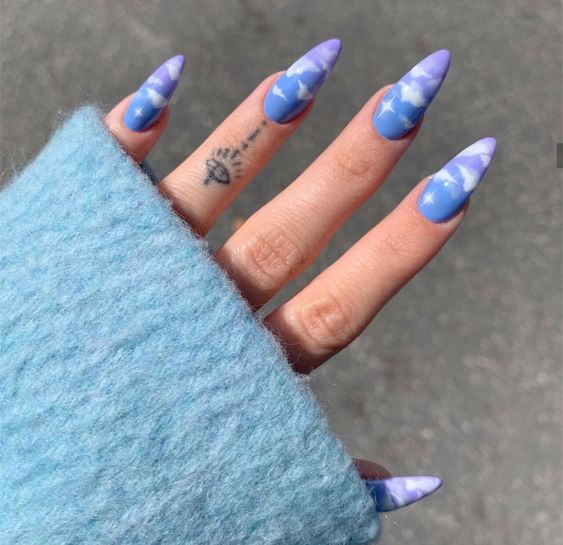 Chica con manicura stiletto en color azul cielo con diseño de nubes blancas