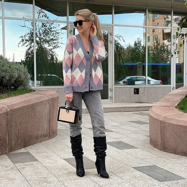 Chica usando un suéter amplio con estampado de rombos de varios colores, jeans y botas negras