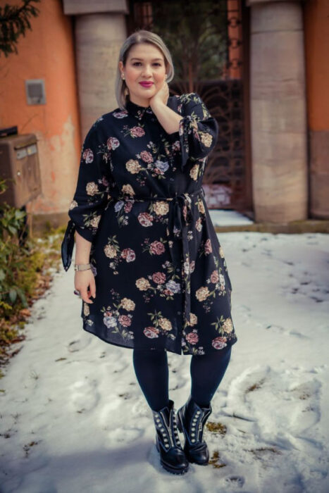 Mujer curvy usando un vestido azul marino de gasa con estampado floral, medias negras y botines negros