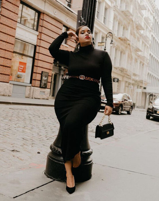 Mujer curvy usando un vestido negro de cuello alto, zapatos de tacón y un cinturón delgado de animal print