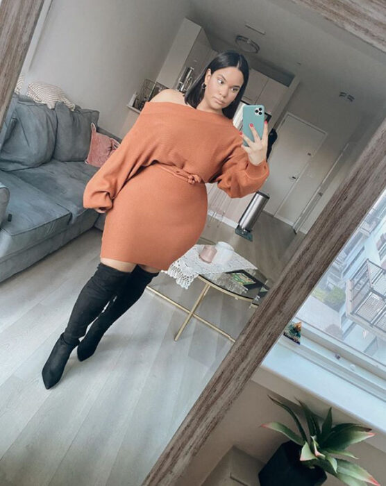 Mujer curvy usando un vestido melocotón, botas altas negras y cinturón