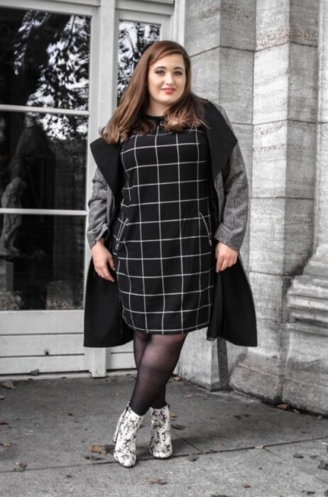 Mujer curvy usando un vestido negro de cuadros blancos, blazer gris, medias negras y botas de pitón