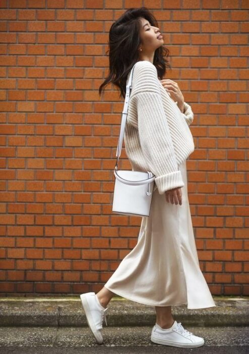 Chica portando un total white look con tenis, falda larga y suéter holgado
