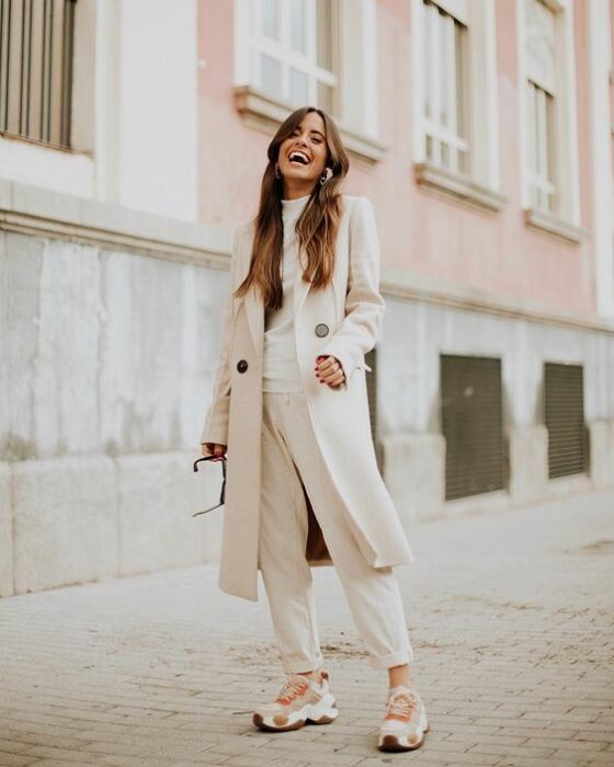 Chica con un total white look de tenis, pantalón de vestir, blusa y abrigo largo