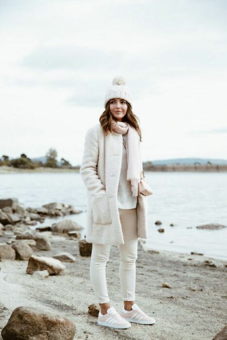 Chica con un total white look que incluye tenis, pantalón, suéter, abrigo largo, bufanda y gorrito