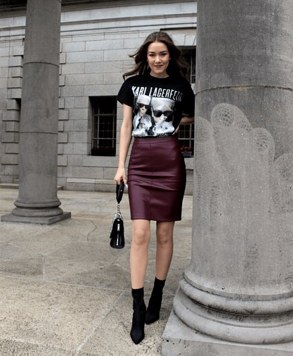 mujer con cabello castaño usando una camiseta negra de karl lagerfeld, minifalda de cuero guinda, botines negros estilo sock boots y bolso de mano negro