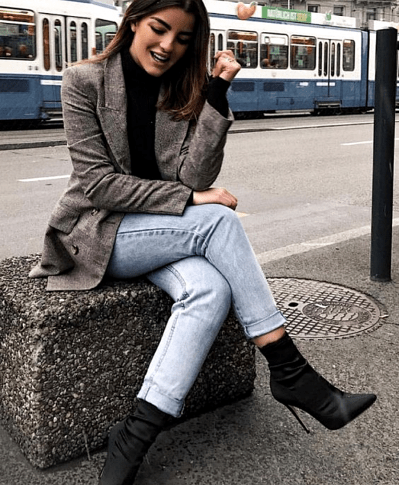 mujer con cabello castaño claro usando un top negro, blazer café tejido, jeans rectos, botines negros estilo sock boots