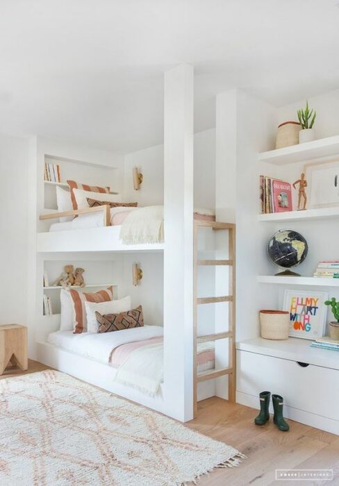 Habitación con paredes blancas y una cama de dos pisos, complementada con alfombra y cojines geométricos