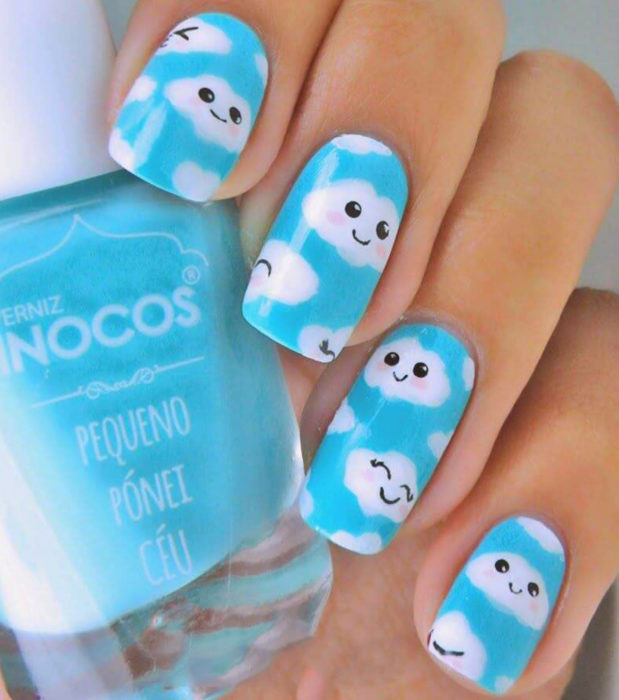 Manicura con diseño de cielo y nubes; uñas cuadradas pintadas con esmalte azul y nube con carita feliz tierna