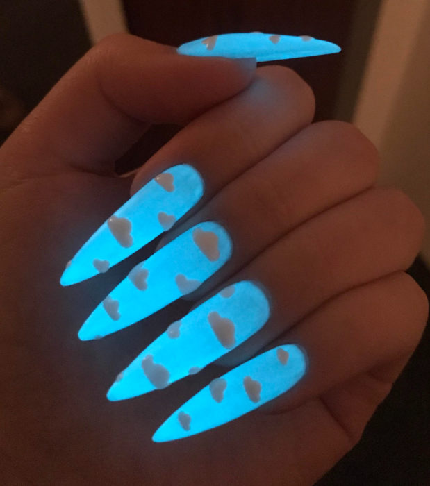 Manicura con diseño de cielo y nubes; uñas largas stiletto pintadas con esmalte azul que brillan en la oscuridad