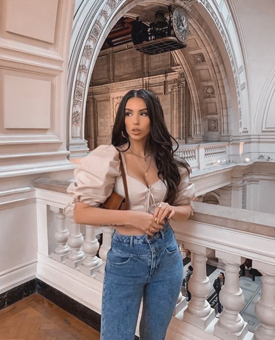 Chica delgada de cabello largo ondulado con jeans de tiro alto y blusa beige claro con mangas abultadas
