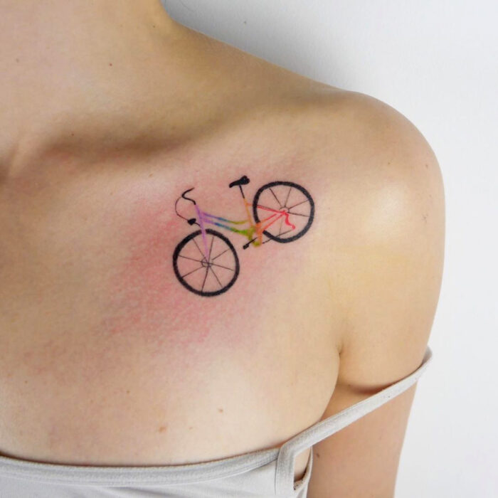 Diseños alegres de tatuajes de bicicleta de colores arcoíris en la clavícula