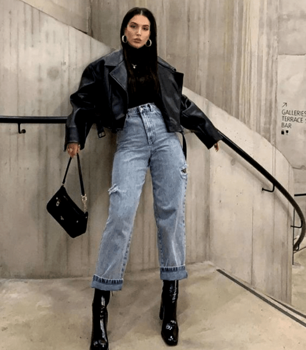 chica de cabello negro usando un top negro, jeans a la cintura holgados, botines negros de tacón, bolso de mano negro