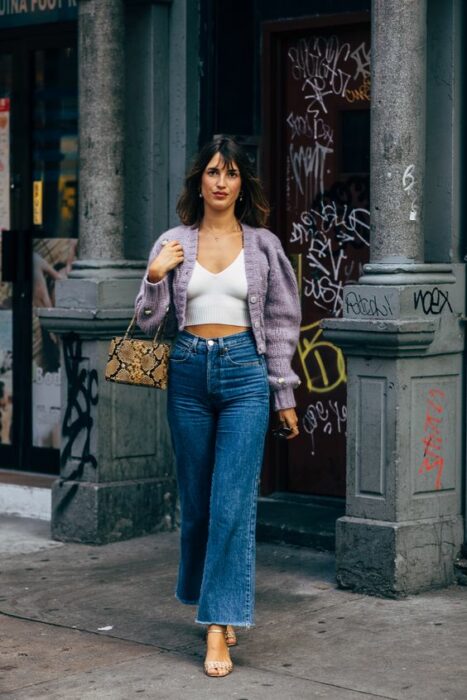 Chica parisina con jeans de campana, sandalias de tacón, blusa blanca y suéter tejido color morado con mangas anchas