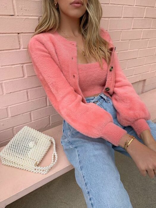 Chica rubia sentada en una banca, vistiendo jeans claros a la cintura con suéter y blusa tejidos con botones cafés