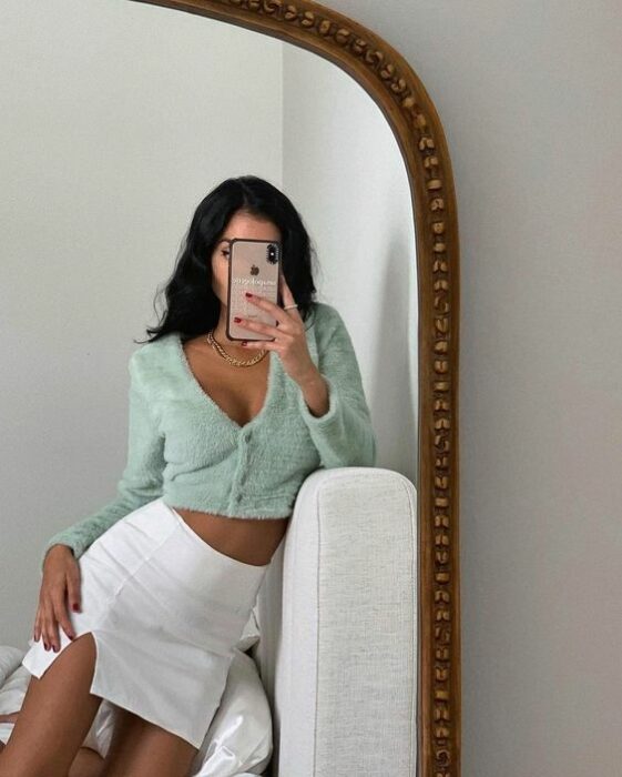 Mujer tomándose una selfie frente al espejo con falda blanca y suéter tejido color verde menta