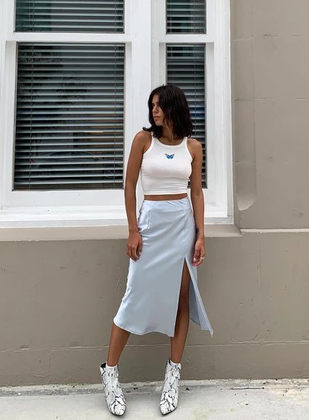 Chica morena posando en la calle con blusa de tirante blanca y falda de satín azul, usando botines de animal print blancos