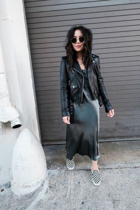 Chica asiática vistiendo chaqueta de cuero y falda de satín negras junto a Vans con cuadros