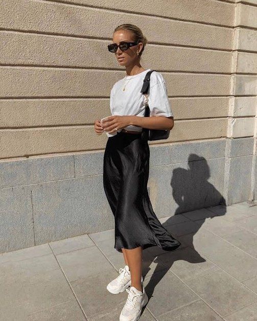 Chica rubia con chongo bajo vistiendo blusa blanca, falda negra de satín, tenis blancos y gafas de sol