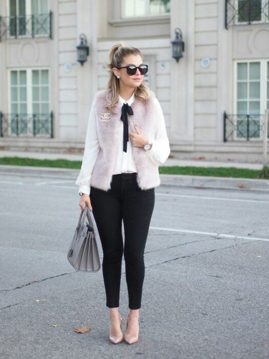 Chica rubia con media coleta y gafas de sol, vistiendo pantalón negro, camisa blanca y abrigo rosa de peluche con un moño negro en el cuello