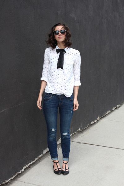 Chica delgada con blusa blanca, jeans oscuros y moño negro en la camisa