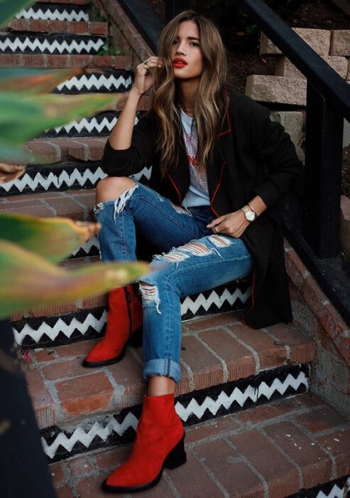 Chica usando blazer negro, playera blanca, jeans rasgados y botines color rojo