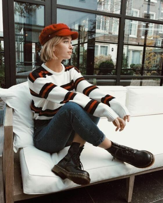 Chica usando boina color rojo, suéter blanco con franjas azul marino y rojas, jeans y botines negros estilo Dr. Martens
