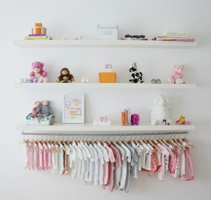 Mini closet usado para colgar la ropa de un bebé, sobre él hay repisas con diferentes juguetes y decoraciones