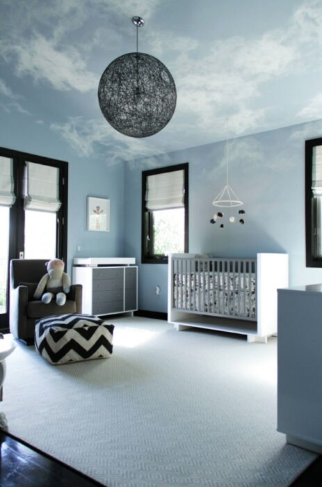Habitación para un bebé decorada en tonos azules con un sofá, cuna y una lámpara en forma de luna