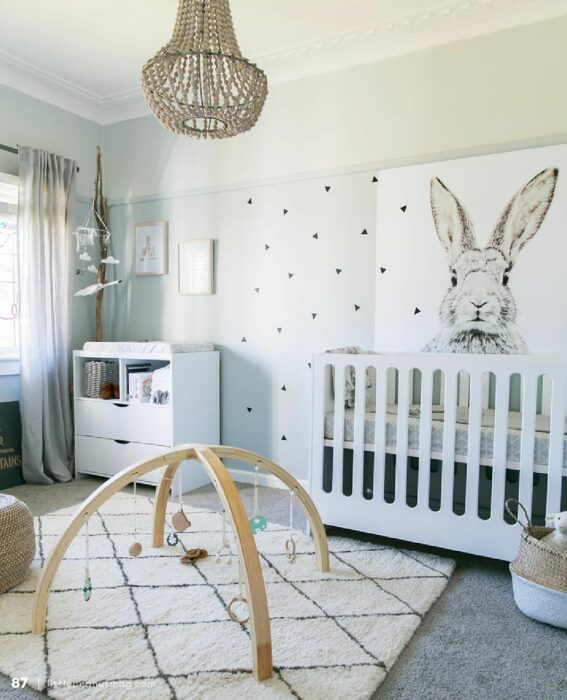 Habitación para un bebé con un móvil de juegos en la alfombra, cuna blanca y un cuadro de conejito