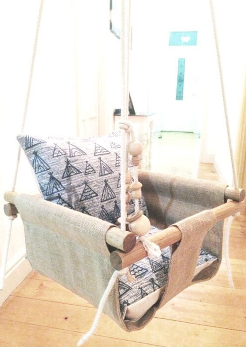 Columpio para bebé, sujeto con cuerdas y decorado con diferentes cojines en color azul y blanco