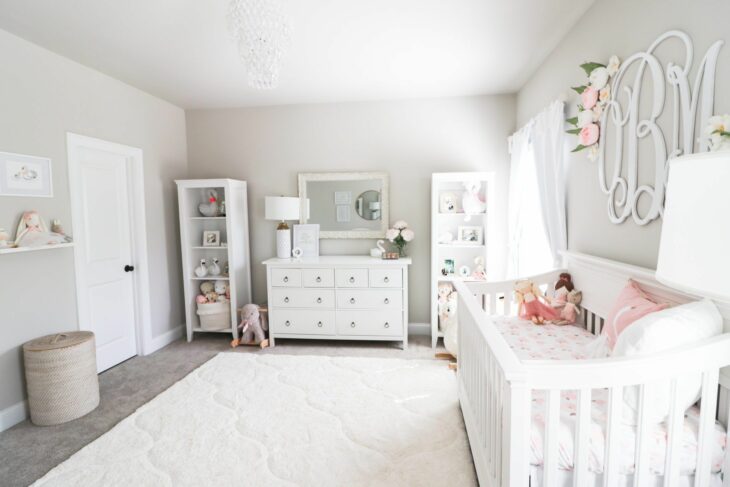 Habitación de un bebé decorada con muebles blancos, cuna, cambiador y una repisa para juguetes