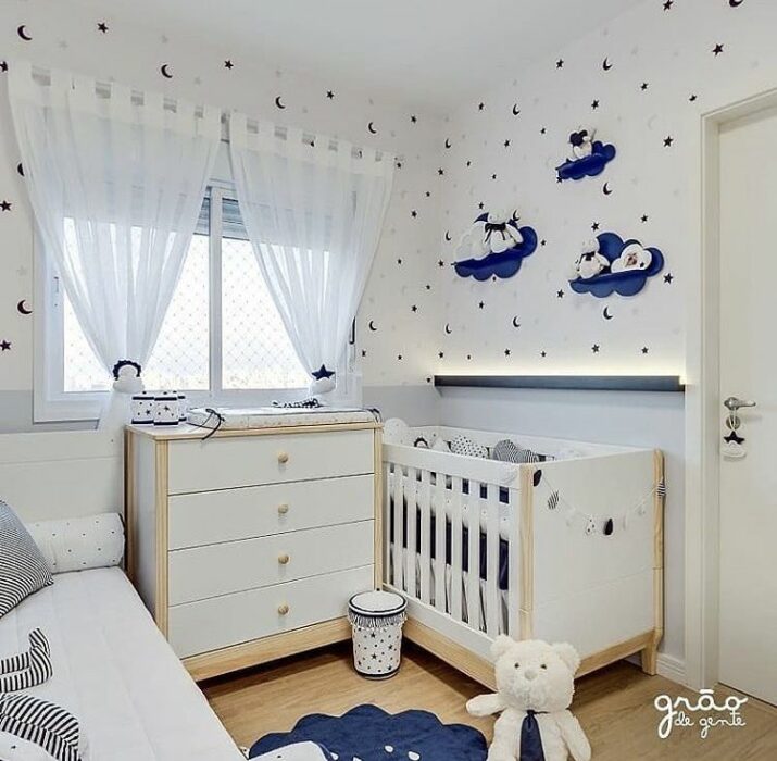 Decoración del cuarto del bebé en tonos azules y blancos con una cama y una cuna separadas por un cambiador en el medio