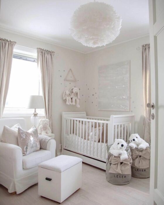 Cuarto de un bebé decorado en blanco, con muebles del mismo color y una lámpara en forma de pelota