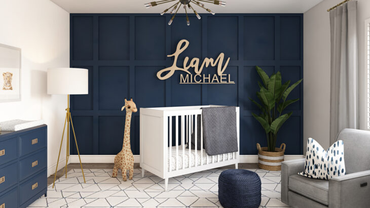 Cuarto del bebé decorado en tonos azul marino, con el nombre en una de las paredes. Cuna blanca, jirafas y un sofá plateado
