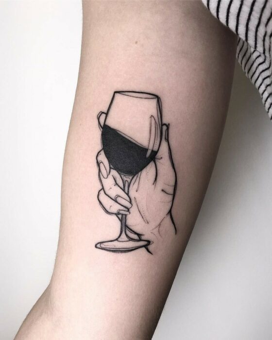 Chica con tatuaje de una mano sosteniendo una copa de vino en el codo