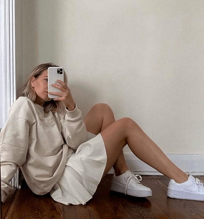 chica rubia usando sudadera oversized beige, falda blanca de tablones, tenis blancos