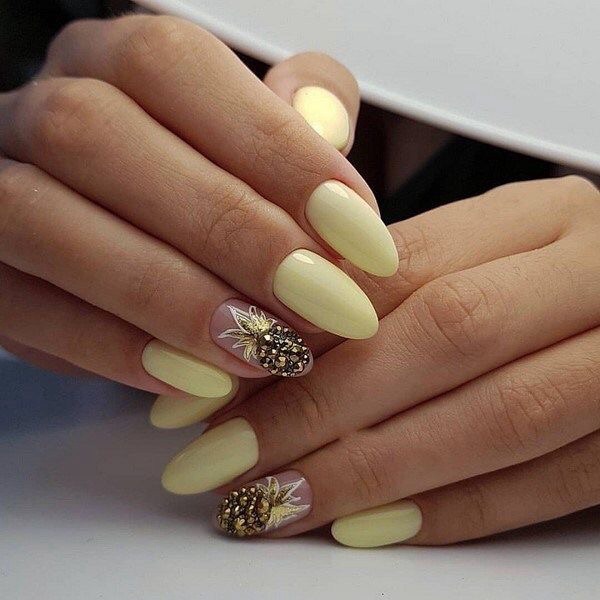 Manicura amarilla pastel con decorado en la punta de perlas doradas en forma de piña