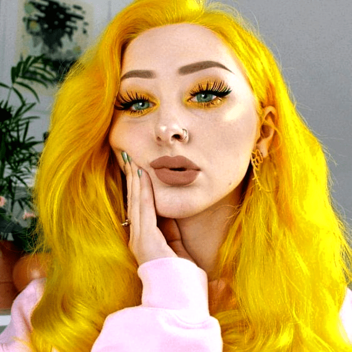 chica de cabello amarillo neón con maquillaje neón, sombras amarillas y pestañas postizas dramáticas