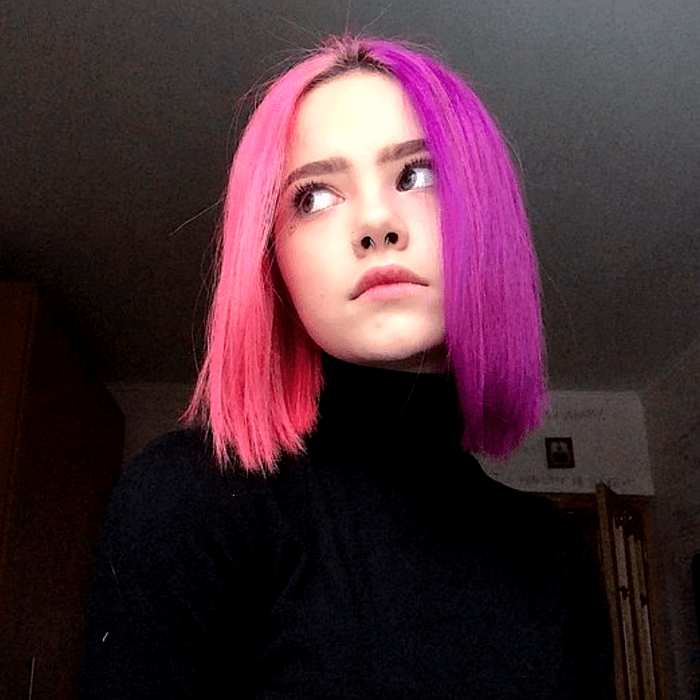chica con cabello corto teñido rosa y morado neón, mitad y mitad. top negro de cuello alto y manga larga