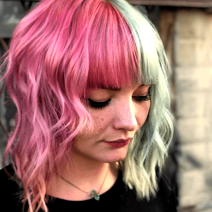 chica de cabello corto teñido rosa y verde pastel, mitad y mitad. usando una camiseta negra de cuello redondo