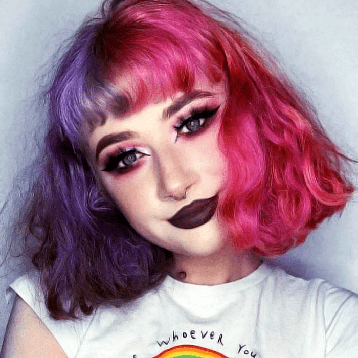 chica de cabello corto con fleco, teñido rosa y morado brillante. usando una camiseta blanca gráfica con estampado de arcoíris