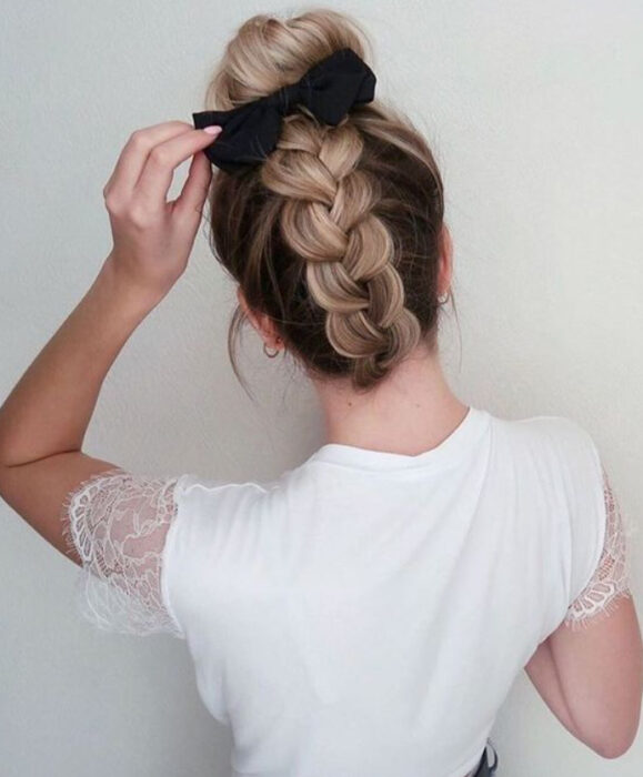 Chica de cabello castaño con trenza en la nuca y moño alto