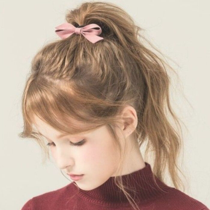 Chica de cabello castaño claro con una coleta desenfadada y un listón rosado