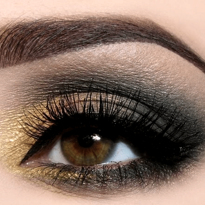 maquillaje de ojos con sombras doradas, grises y negras, además de delineador negro y pestañas postizas