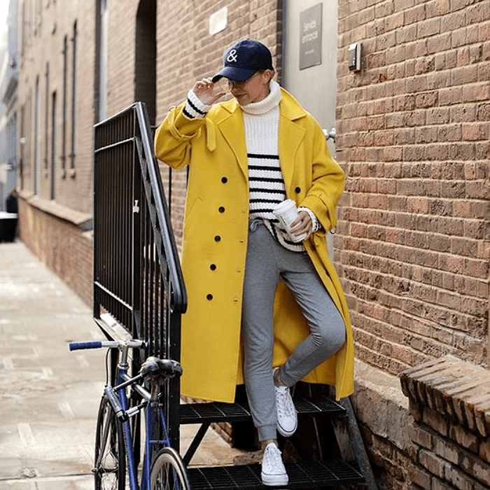 mujer con gorra azul y abrigo amarillo, combinando con un suéter blanco