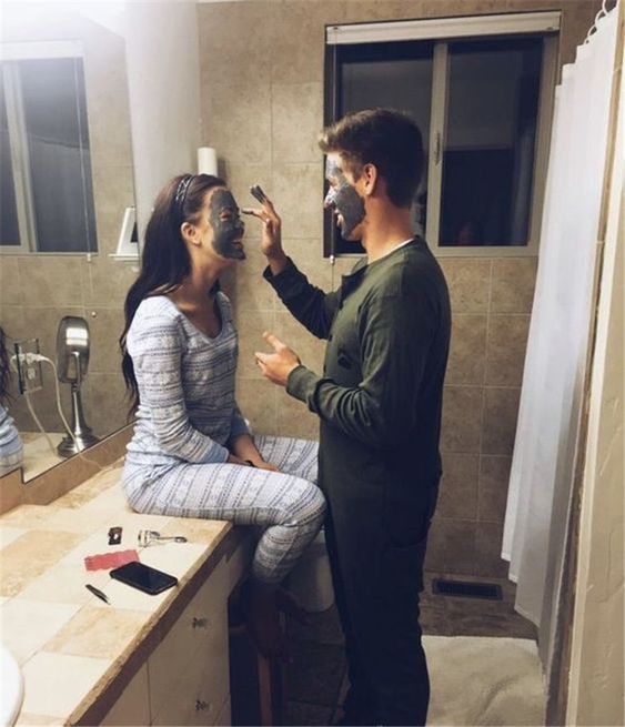 Chico poniendo una mascarilla a su novia mientras están en el cuarto de una habitación