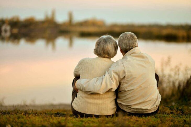 Pareja de ancianos sentados frente a un lago viendo el atardecer